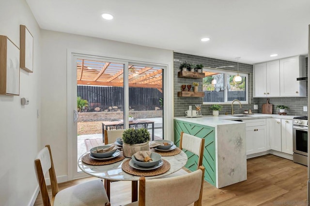 kitchen featuring sink, white cabinets, hanging light fixtures, stainless steel range oven, and light hardwood / wood-style flooring