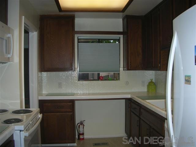 kitchen featuring backsplash, white appliances, and dark brown cabinetry