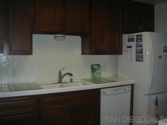 kitchen with sink, dark brown cabinets, tasteful backsplash, and white appliances