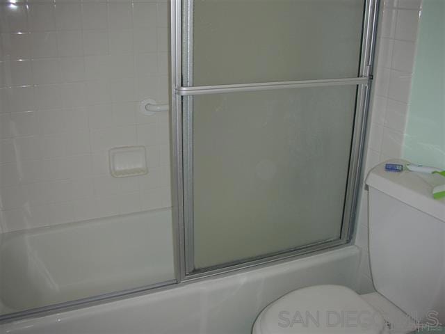 bathroom featuring bath / shower combo with glass door and toilet