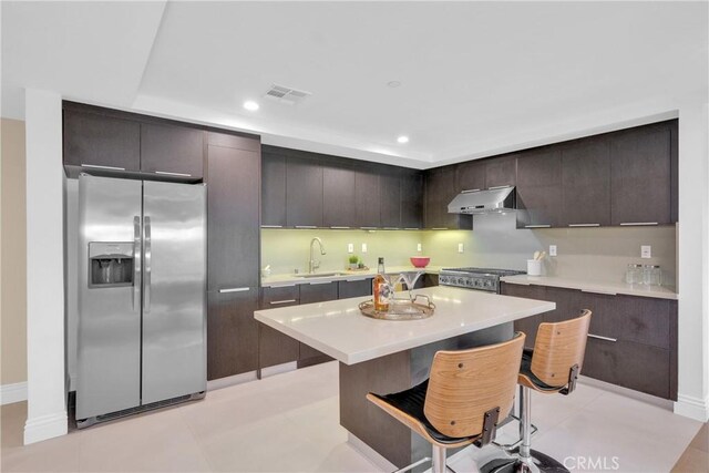 kitchen featuring dark brown cabinetry, a center island, stainless steel refrigerator with ice dispenser, sink, and a breakfast bar area