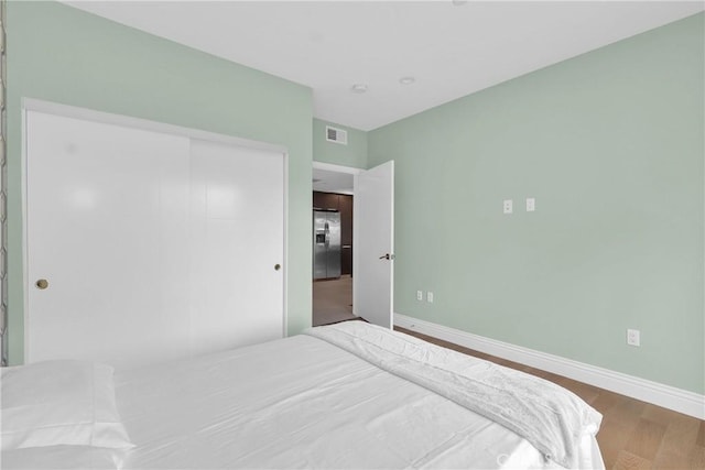 bedroom with stainless steel refrigerator with ice dispenser, hardwood / wood-style floors, and a closet