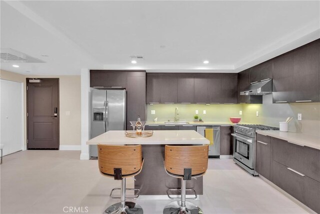 kitchen featuring a center island, sink, dark brown cabinetry, appliances with stainless steel finishes, and a breakfast bar area