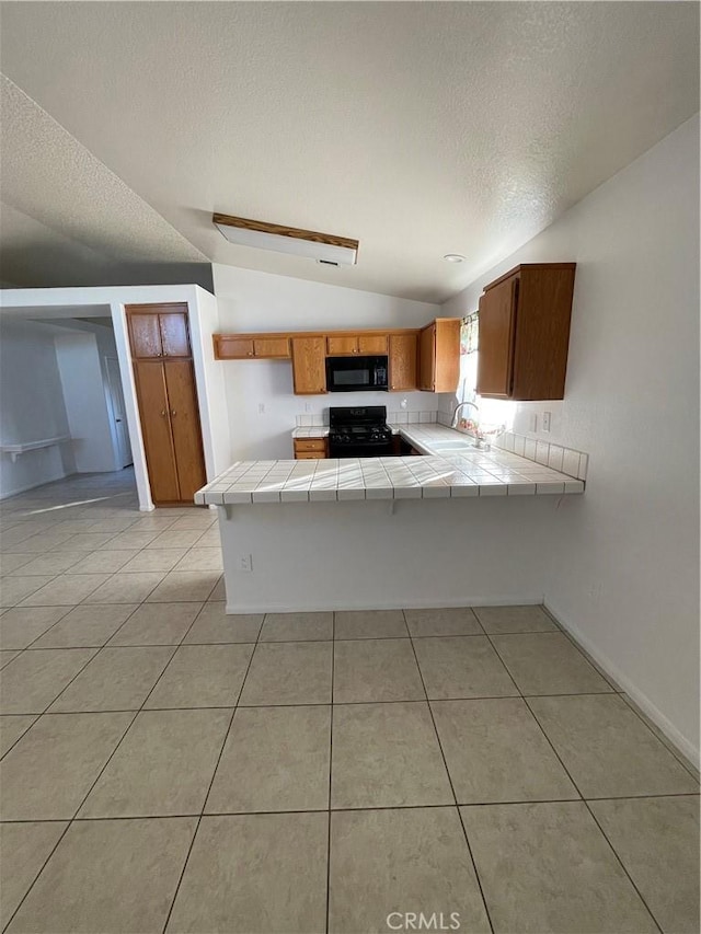 kitchen with black appliances, lofted ceiling, kitchen peninsula, tile countertops, and light tile patterned floors