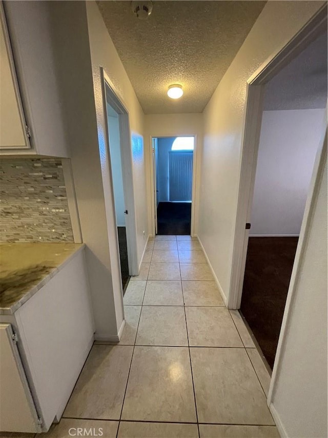 corridor featuring a textured ceiling and light tile patterned floors