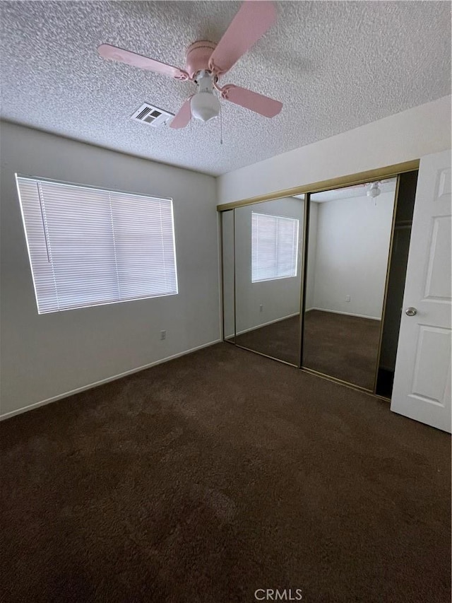 unfurnished bedroom with a textured ceiling, ceiling fan, a closet, and dark colored carpet