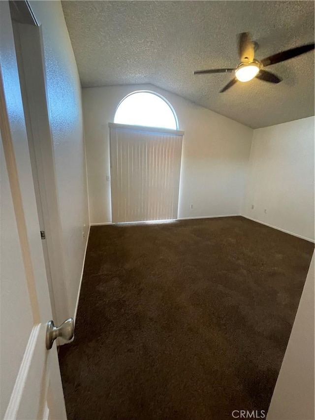 unfurnished room with ceiling fan, dark carpet, and a textured ceiling