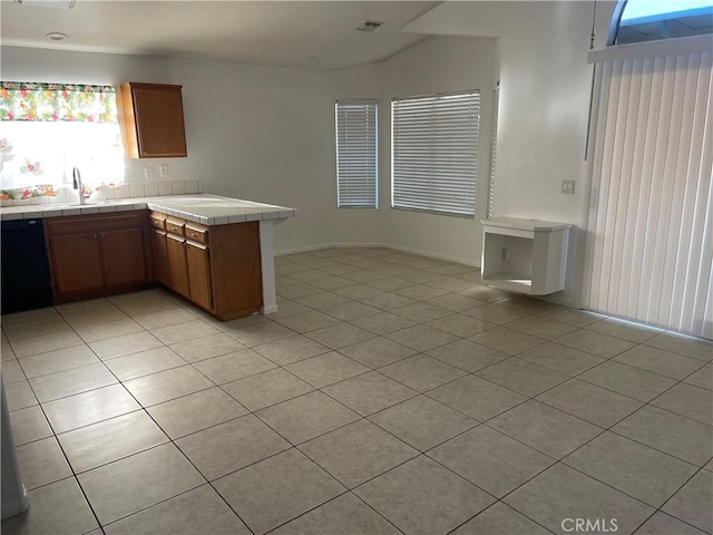 kitchen with light tile patterned floors, kitchen peninsula, tile counters, black dishwasher, and sink