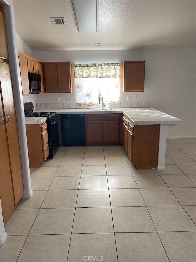 kitchen featuring sink, light tile patterned floors, black appliances, and tile countertops