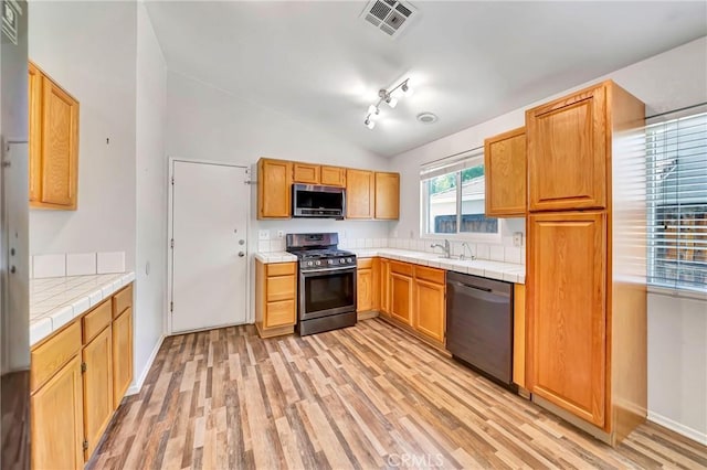 kitchen featuring appliances with stainless steel finishes, tile counters, light wood-type flooring, track lighting, and lofted ceiling