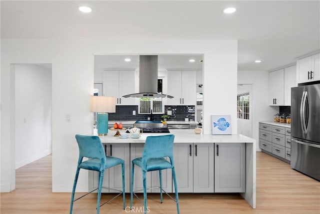 kitchen featuring a kitchen bar, gray cabinetry, island range hood, stainless steel fridge, and white cabinets