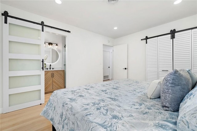 bedroom with wood-type flooring, a barn door, and connected bathroom