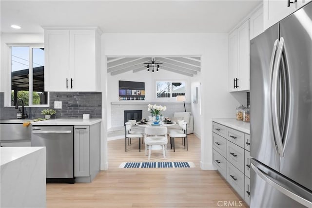 kitchen featuring tasteful backsplash, white cabinetry, lofted ceiling with beams, stainless steel appliances, and light hardwood / wood-style flooring