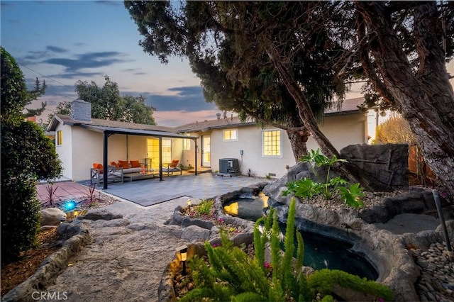 back house at dusk with an outdoor living space, a patio, and central AC unit