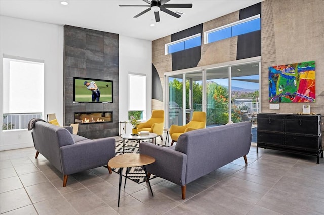 living room with ceiling fan, a towering ceiling, and a fireplace