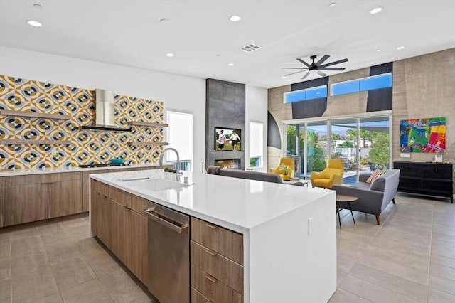 kitchen featuring dishwasher, range hood, a center island with sink, a large fireplace, and sink