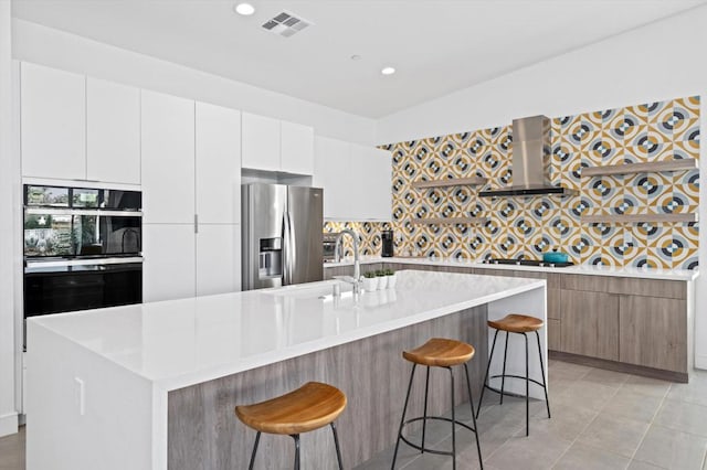 kitchen with white cabinets, stainless steel appliances, a kitchen island with sink, a breakfast bar, and range hood