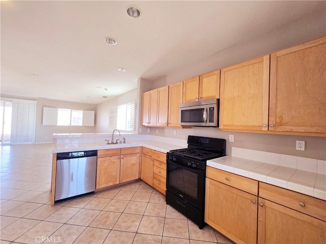 kitchen with light tile patterned flooring, appliances with stainless steel finishes, tile counters, and sink