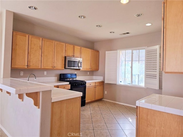 kitchen with light tile patterned flooring, a breakfast bar area, tile counters, black gas stove, and kitchen peninsula