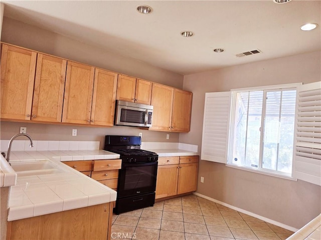 kitchen with light tile patterned flooring, sink, tile countertops, and black gas range