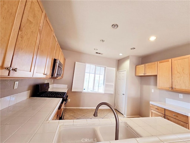 kitchen featuring black range with gas stovetop, tile counters, sink, and light brown cabinets