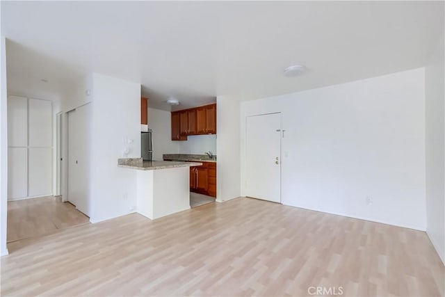 kitchen with kitchen peninsula, stainless steel refrigerator, light hardwood / wood-style flooring, and sink