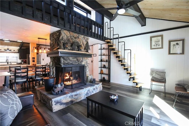 living room with ceiling fan, wood-type flooring, a fireplace, and vaulted ceiling with beams