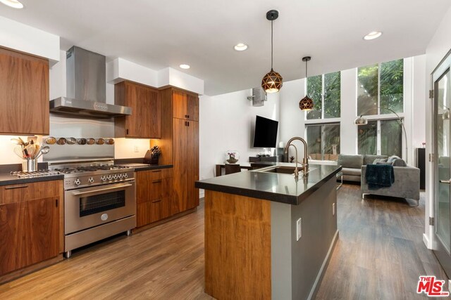 kitchen with high end range, dark hardwood / wood-style floors, wall chimney exhaust hood, and an island with sink