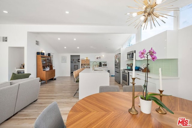 dining space with sink, light hardwood / wood-style floors, lofted ceiling with beams, and a notable chandelier