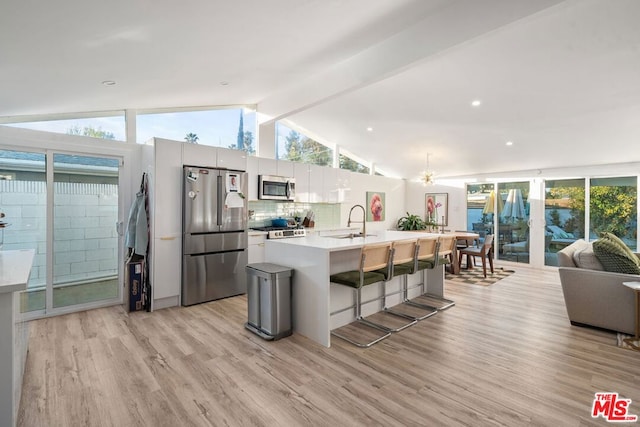 kitchen featuring tasteful backsplash, a center island with sink, appliances with stainless steel finishes, a kitchen breakfast bar, and white cabinets