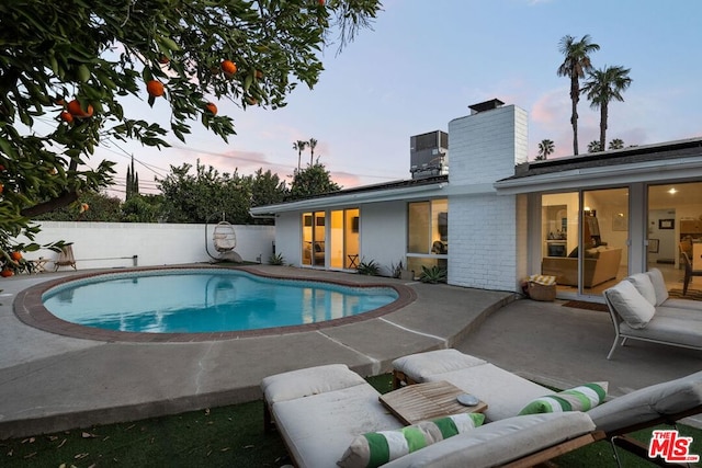 pool at dusk featuring a patio area and cooling unit