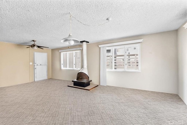 unfurnished living room with a textured ceiling, ceiling fan, carpet, and a wood stove