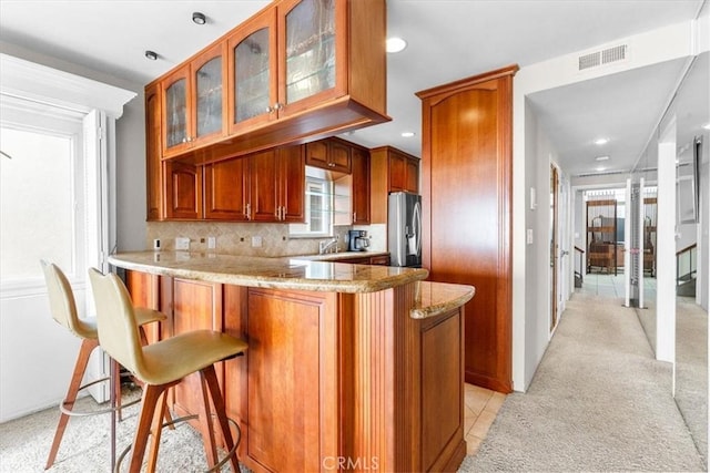 kitchen featuring kitchen peninsula, stainless steel refrigerator with ice dispenser, a breakfast bar area, tasteful backsplash, and light stone counters