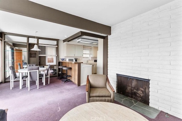 living room featuring beam ceiling, a brick fireplace, brick wall, and dark carpet