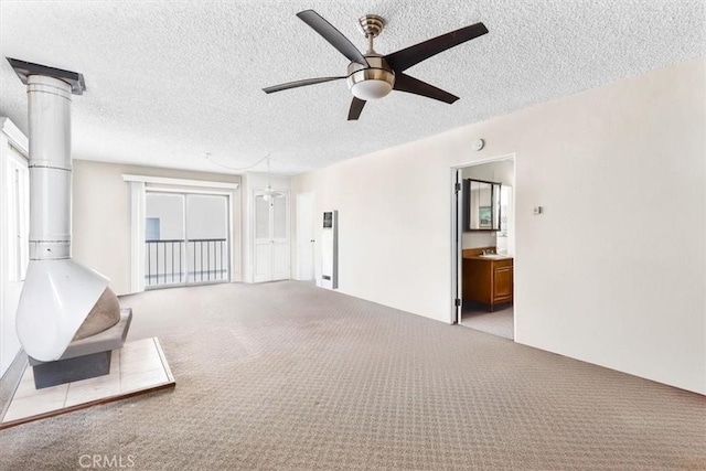 unfurnished living room with a wood stove, ceiling fan, a textured ceiling, and light colored carpet