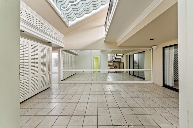 spare room featuring vaulted ceiling, light tile patterned flooring, crown molding, and stairway