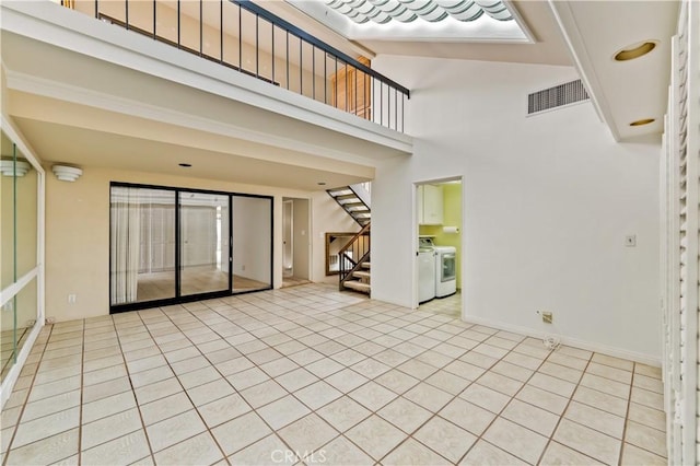 interior space featuring light tile patterned floors, visible vents, a towering ceiling, independent washer and dryer, and stairs