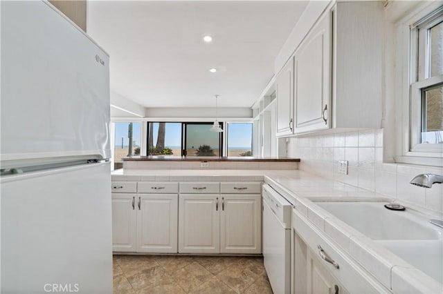 kitchen featuring white appliances, white cabinets, a peninsula, light countertops, and a sink