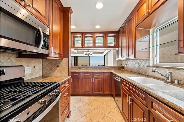 kitchen with brown cabinets, light tile patterned floors, stainless steel appliances, a sink, and light stone countertops