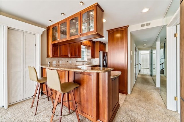 kitchen featuring visible vents, glass insert cabinets, light stone counters, a peninsula, and stainless steel refrigerator with ice dispenser