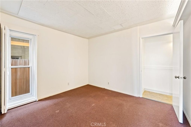 empty room with a textured ceiling, dark carpet, and baseboards