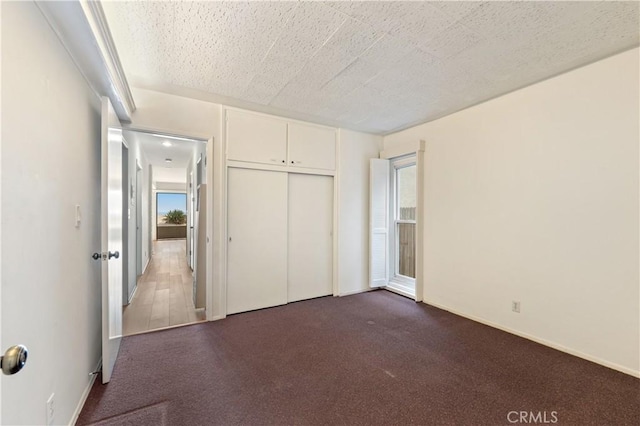 unfurnished bedroom featuring a textured ceiling, dark colored carpet, and a closet