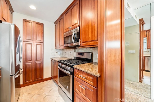 kitchen featuring stainless steel appliances, light tile patterned flooring, backsplash, and light stone counters