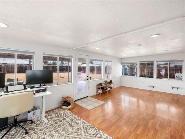 office area with light hardwood / wood-style floors, a textured ceiling, and a healthy amount of sunlight