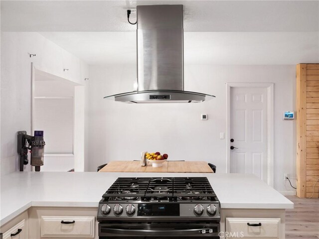 kitchen with light hardwood / wood-style floors, kitchen peninsula, island exhaust hood, and gas stove