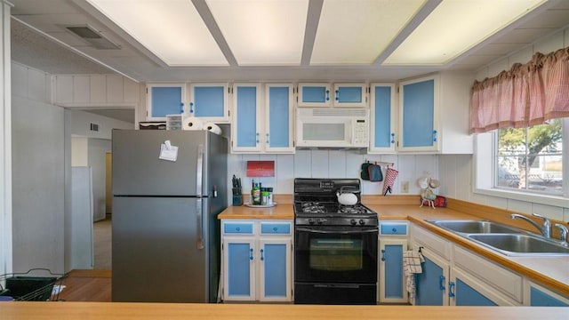 kitchen with sink, stainless steel fridge, black gas range oven, and blue cabinetry