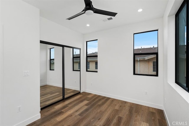 unfurnished bedroom featuring ceiling fan, dark wood-type flooring, multiple windows, and a closet