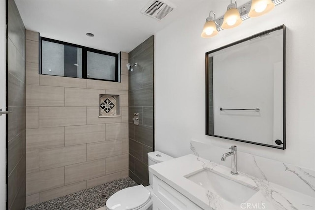 bathroom with toilet, vanity, and tiled shower