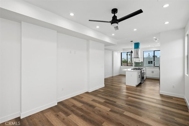 kitchen with decorative light fixtures, a kitchen island, white cabinetry, wall chimney exhaust hood, and gas range