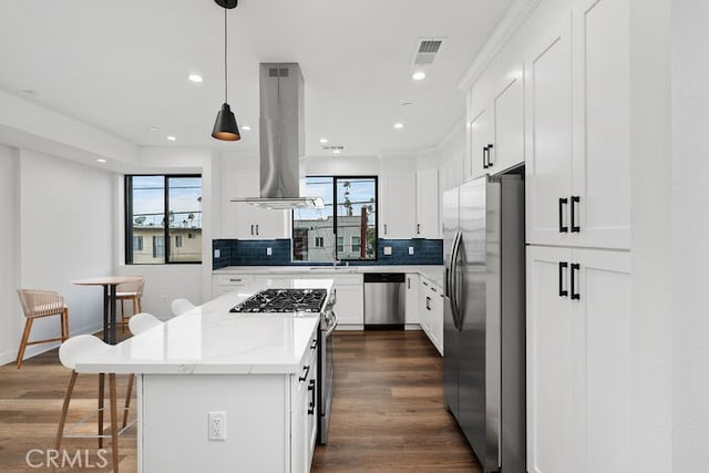 kitchen featuring pendant lighting, a kitchen island, white cabinetry, stainless steel appliances, and island range hood